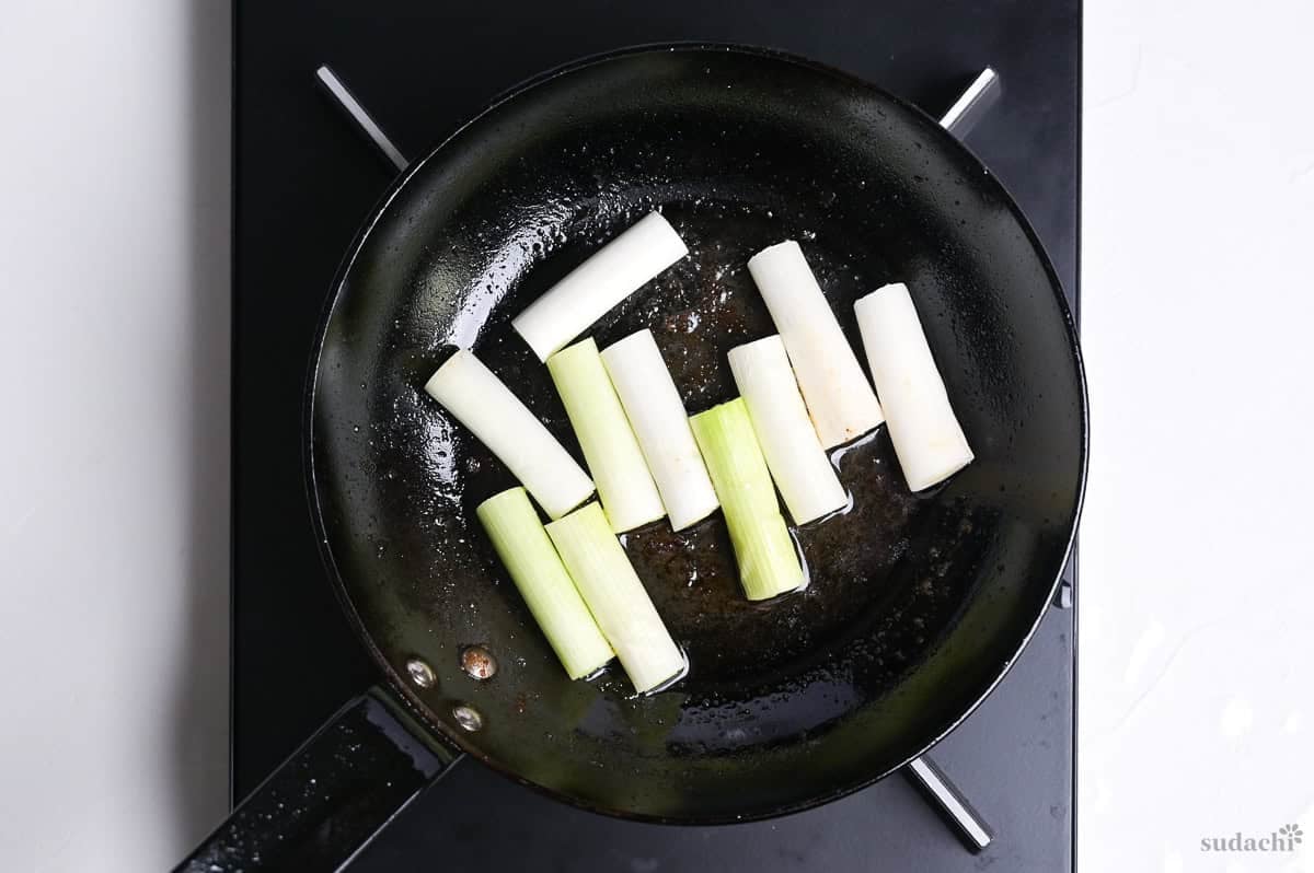 frying Japanese leek in duck fat in a pan on the stove top