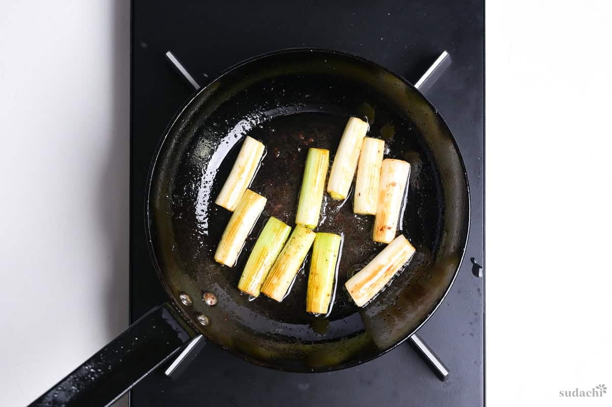 lightly charred Japanese leek in a frying pan on the stove top