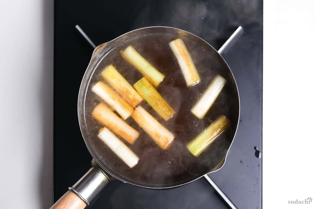 Broth for kamo nanban soba with pieces of charred Japanese leek simmering in a pot on the stove top