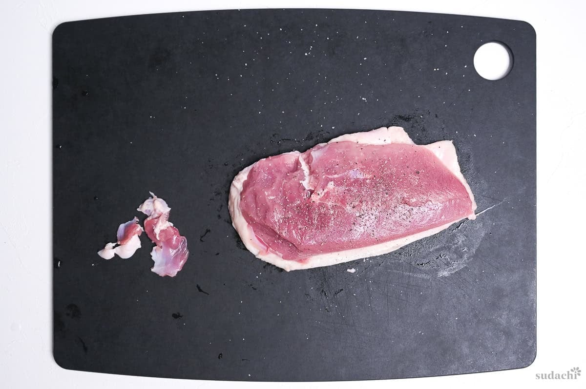 duck breast seasoned with salt and ground black pepper on a black cutting board