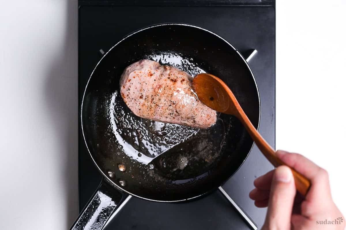 basting flesh side of duck breast with rendered fat in a frying pan on the stove