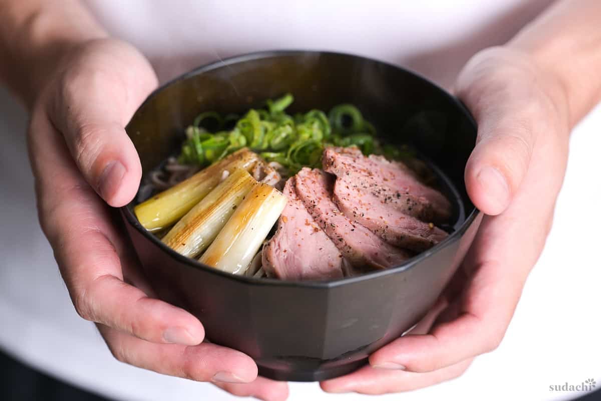 Yuto Omura holding a bowl of duck soba noodle soup with Japanese leek