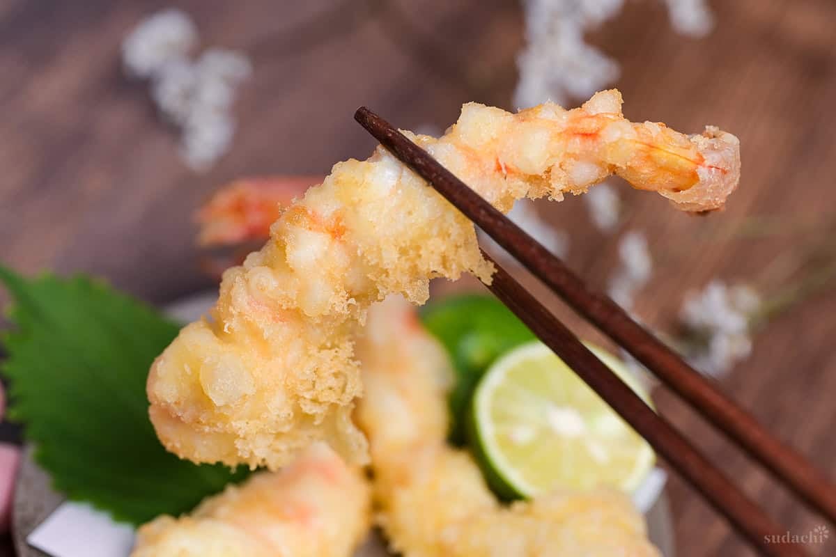 homemade ebiten (prawn tempura) held up with dark wooden chopsticks