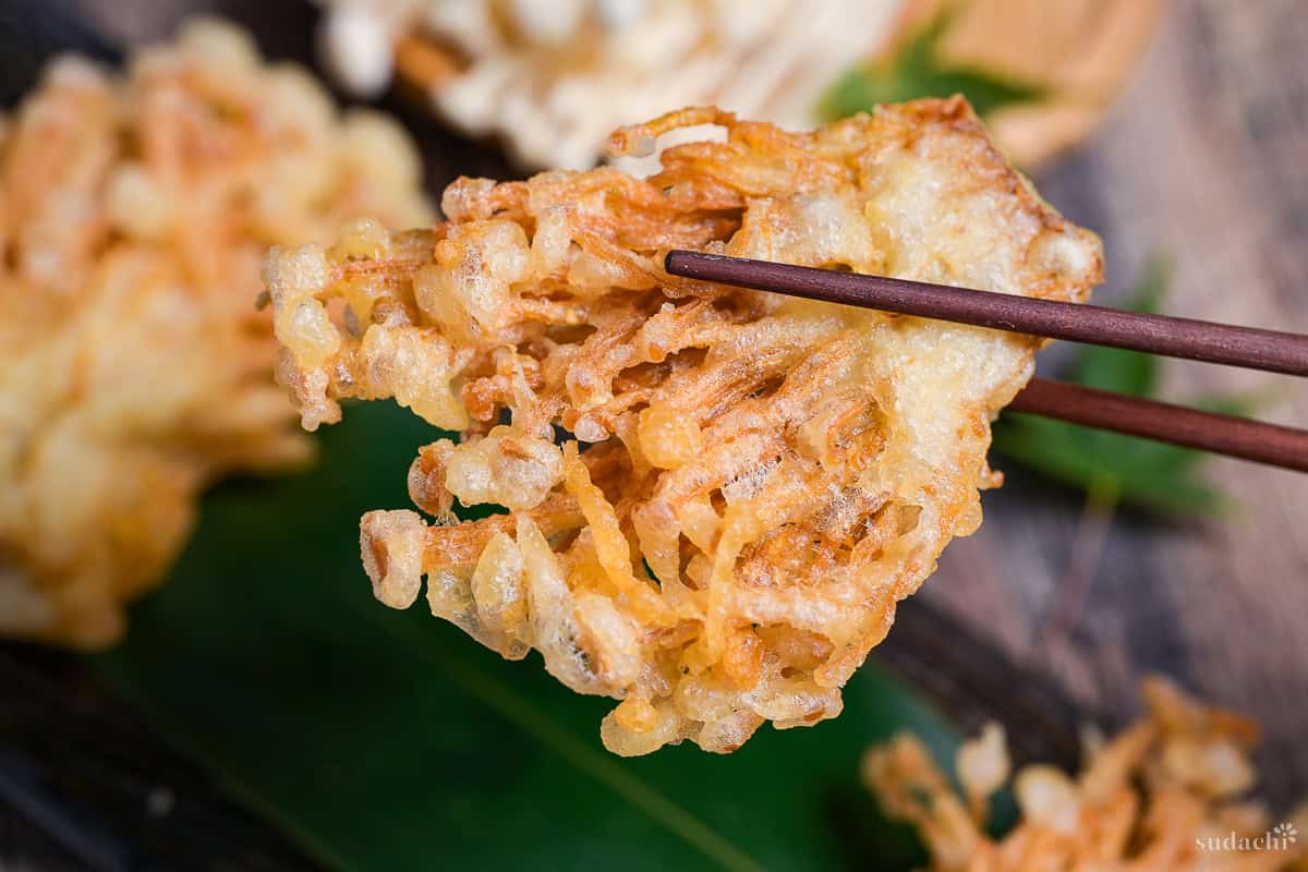 enoki tempura held up with wooden chopsticks