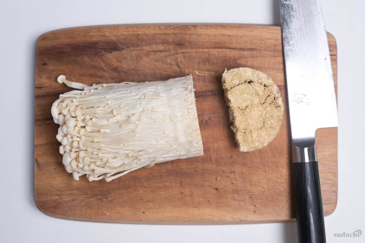 enoki mushrooms on a wooden cutting board with the base cut off next to a Japanese knife