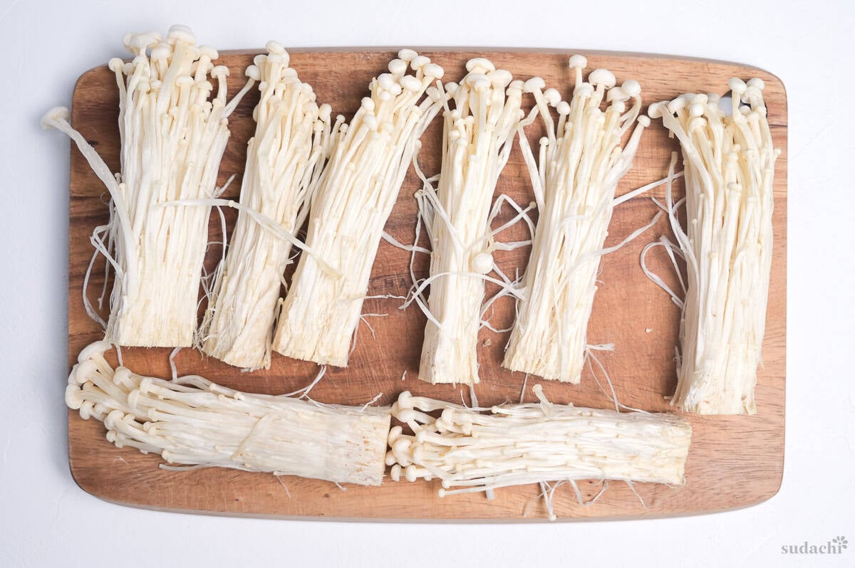 A bunch of enoki mushrooms divided into small bundles on a wooden cutting board