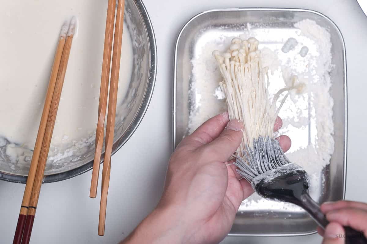 using a pastry brush to coat a small bunch of enoki mushrooms with starch