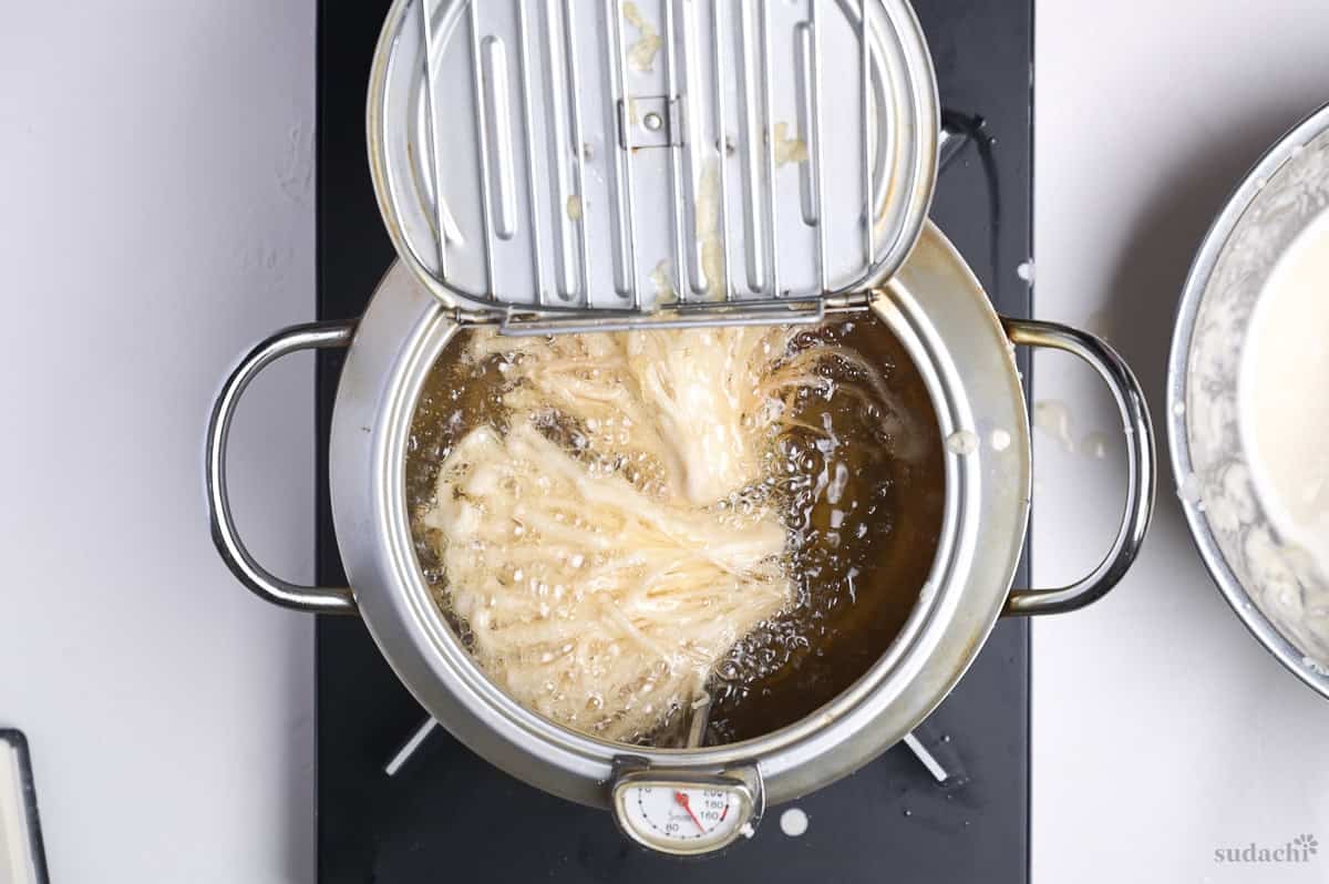 enoki tempura frying in a pot of oil on the stove top