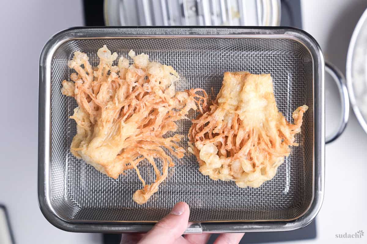 fried enoki mushroom tempura resting on a mesh wire rack to drain excess oil