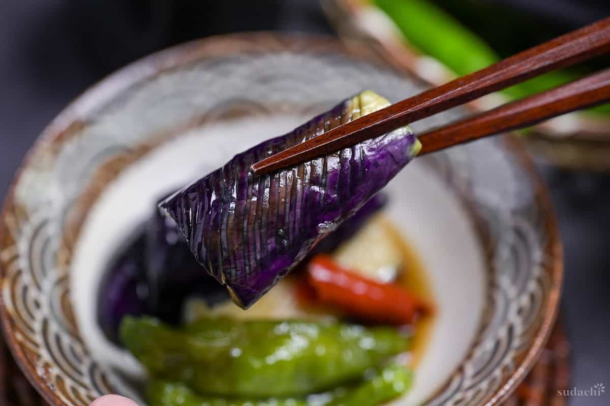 Close up of eggplant agebitashi held up with dark wooden chopsticks