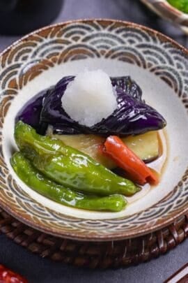 Nasu no agebitashi (Fried Japanese eggplant in dashi) with shishito peppers and chili topped with grated daikon radish in a dish with brown and grayish blue seigaiha pattern