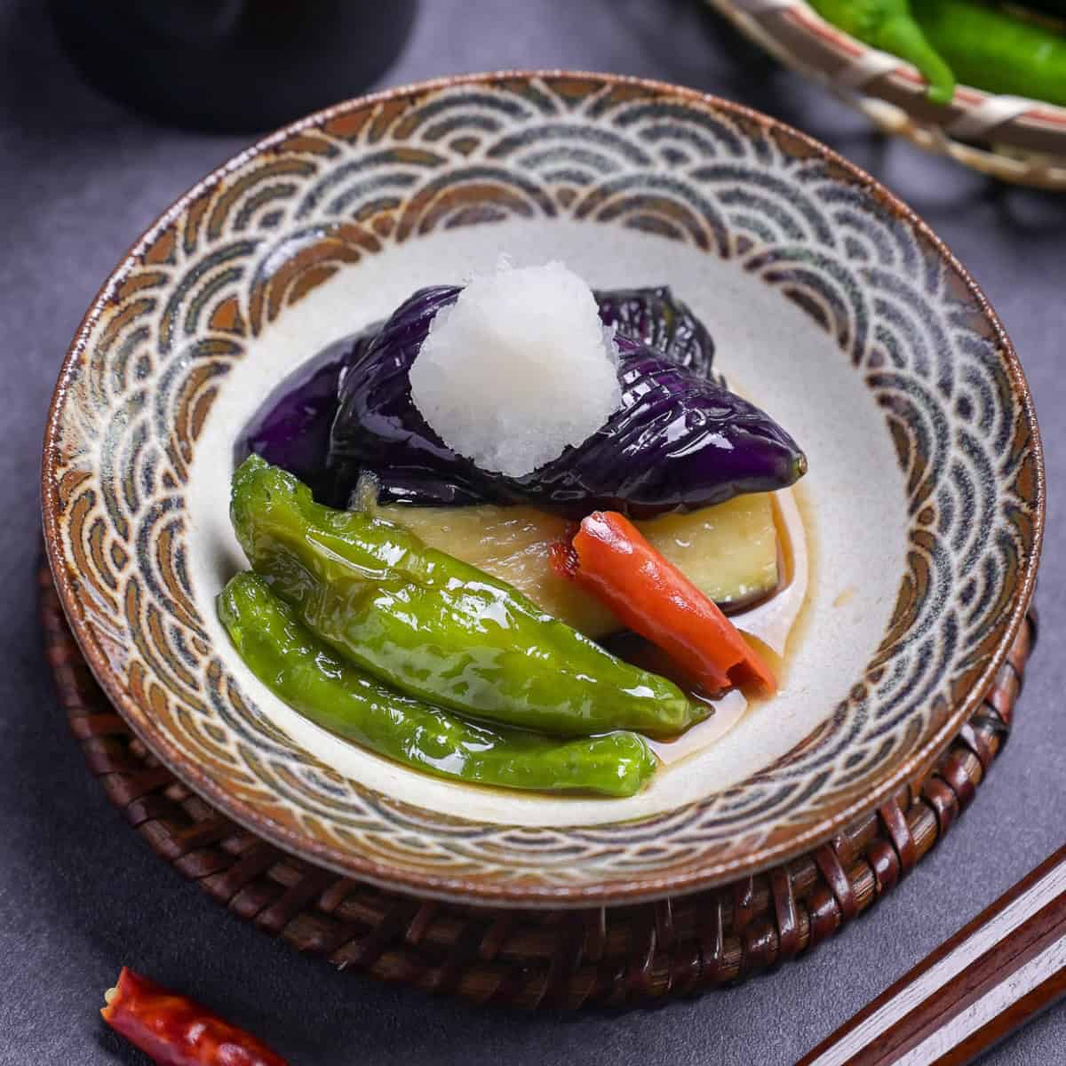 Nasu no agebitashi (Fried Japanese eggplant in dashi) with shishito peppers and chili topped with grated daikon radish in a dish with brown and grayish blue seigaiha pattern