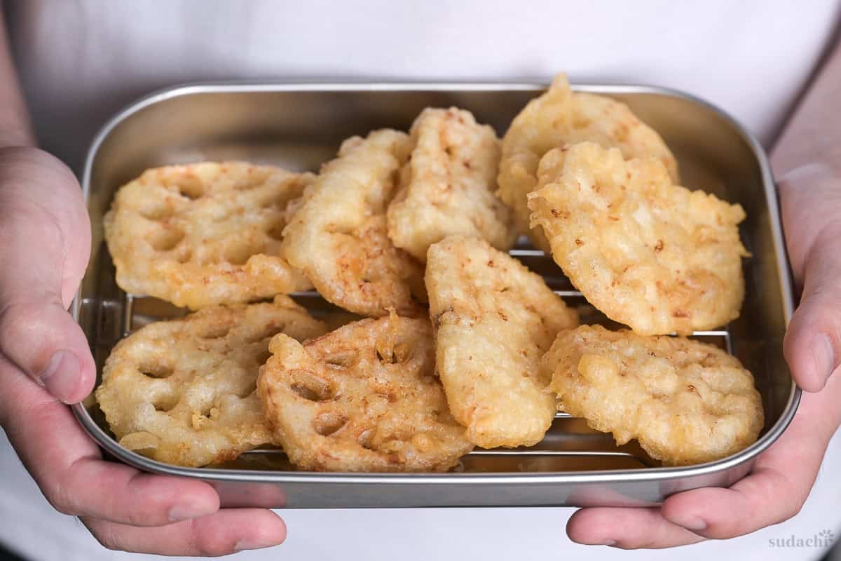 Yuto Omura holding renkon (lotus root) tempura on a wire rack in a steel prep container