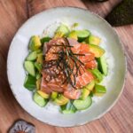 marinated salmon sashimi bowl with cucumber and avocado topped with sesame seeds and kizami nori in a mottled gray ceramic bowl