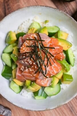 marinated salmon sashimi bowl with cucumber and avocado topped with sesame seeds and kizami nori in a mottled gray ceramic bowl