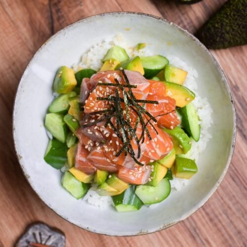 marinated salmon sashimi bowl with cucumber and avocado topped with sesame seeds and kizami nori in a mottled gray ceramic bowl