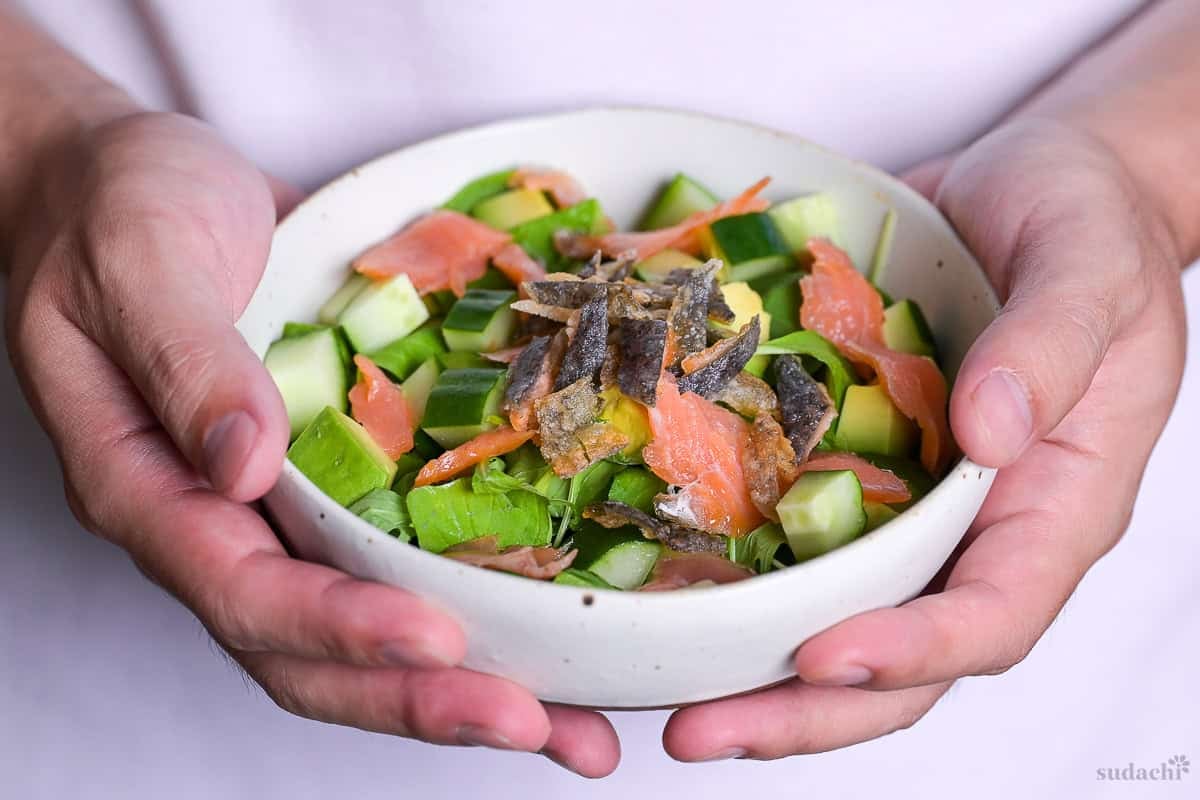 Yuto Omura holding up salmon skin salad in a white speckled bowl.