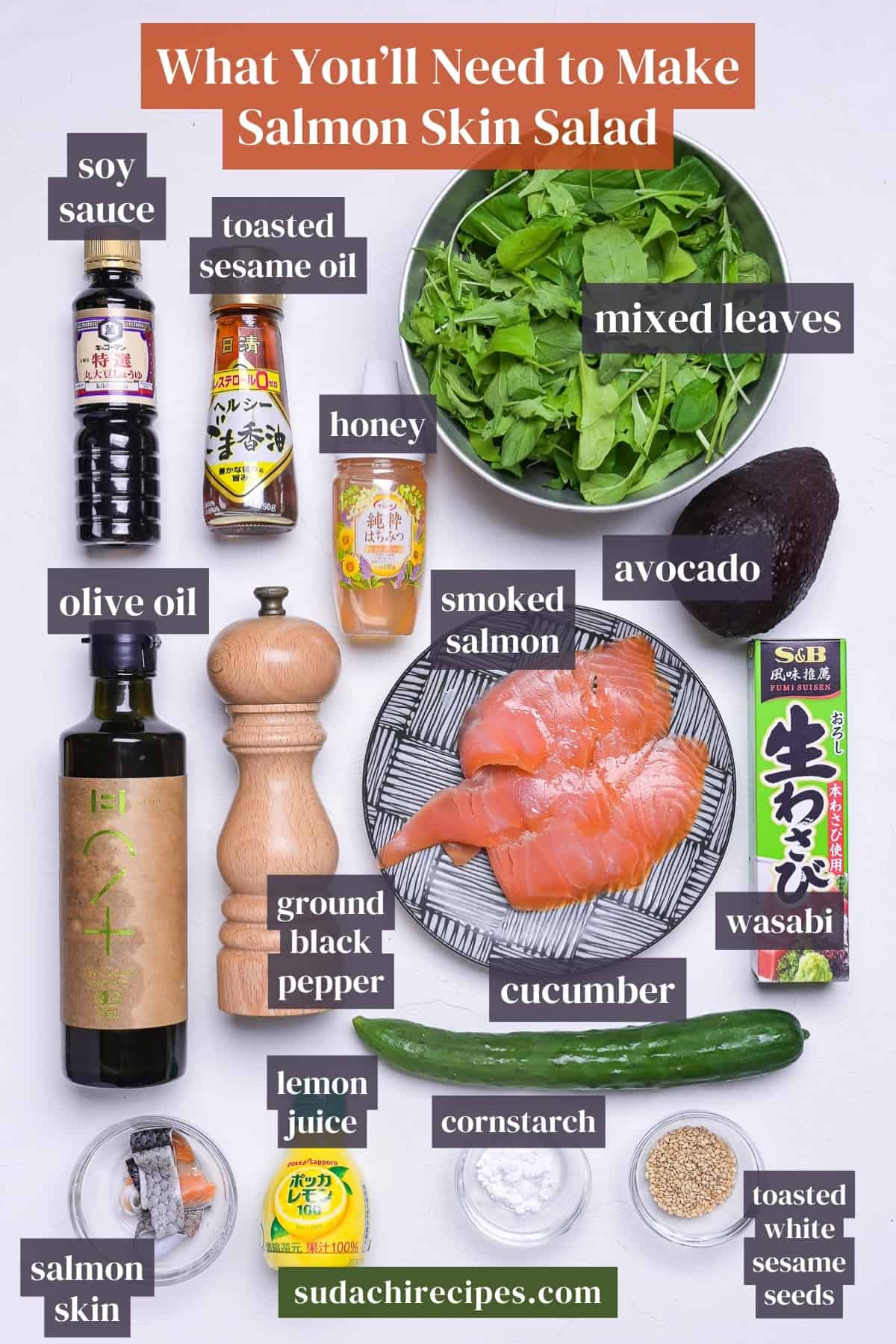 Ingredients needed to make salmon skin salad on a white background with labels. From top to bottom, left to right: soy sauce, toasted sesame oil, mixed leaves, honey, olive oil, smoked salmon, avocado, ground black pepper, cucumber, wasabi, salmon skin, lemon juice, cornstarch, toasted shite sesame seeds.