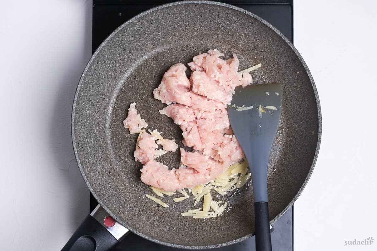 Raw ground chicken and julienned ginger in a frying pan to make soboro for sanshoku donburi.