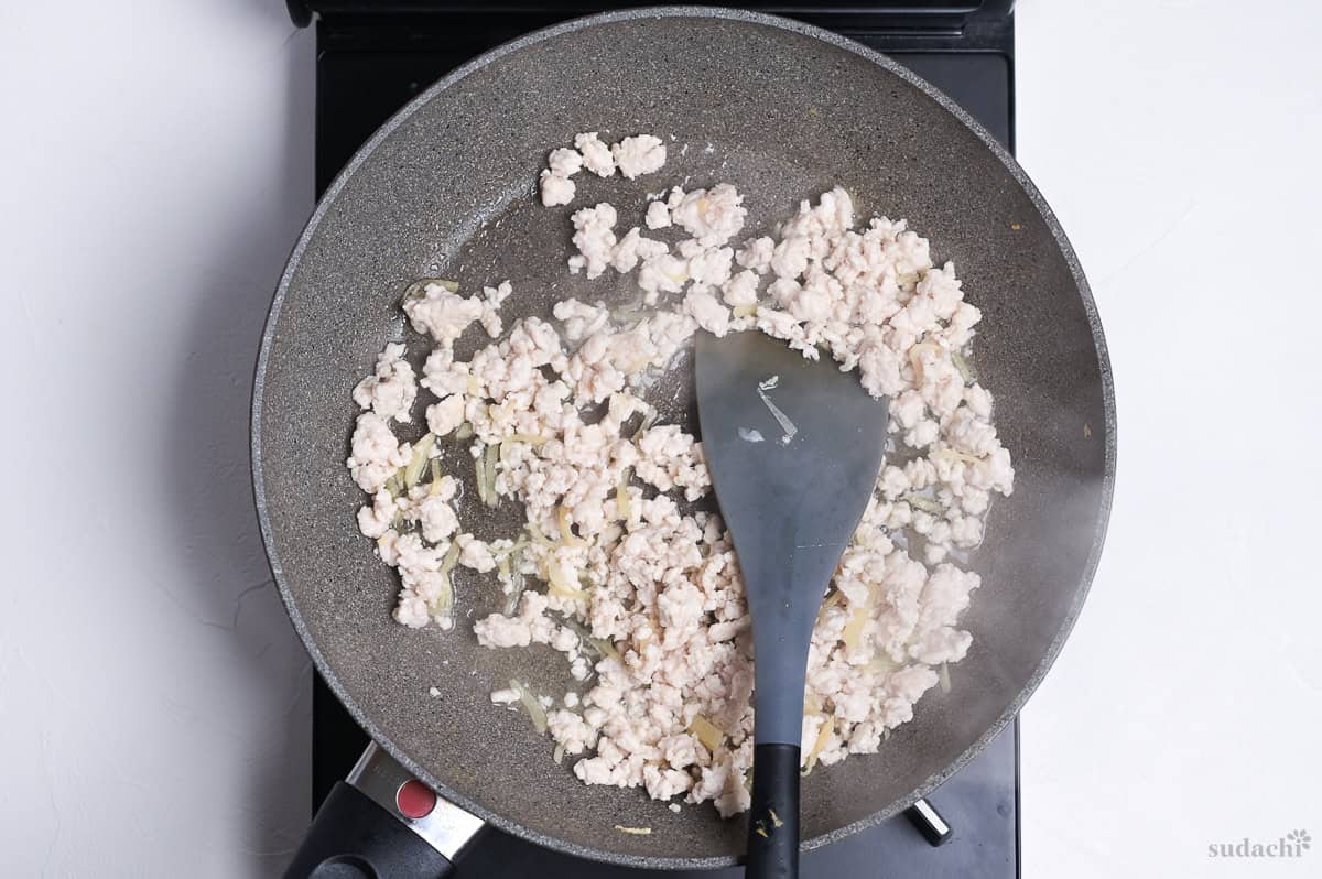 Ground chicken and ginger frying in a pan on the stove top.