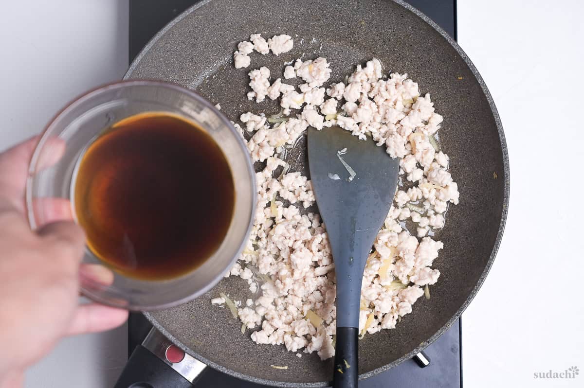 Pouring sauce over cooked ground chicken in a frying pan to make sanshoku soboro don