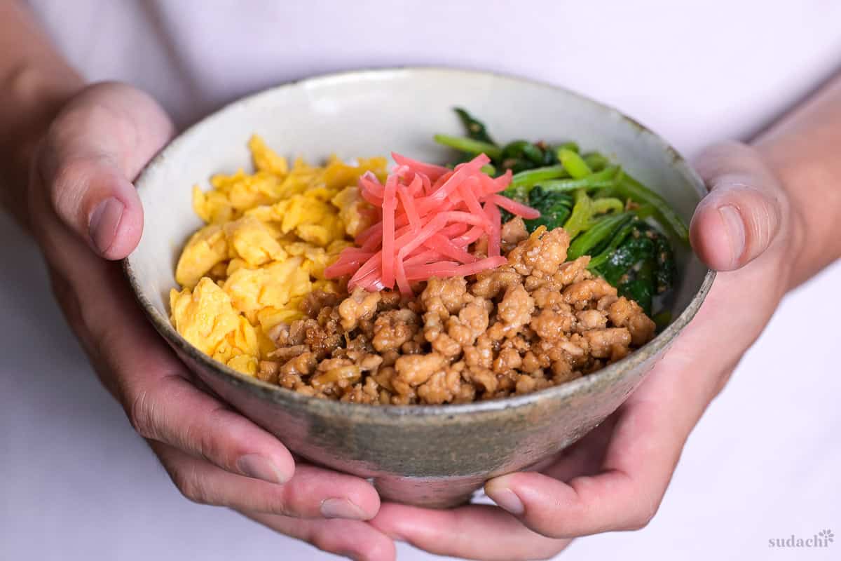 Yuto Omura holding up sanshoku soboro don made with ground chicken, egg and spinach topped with pink pickled ginger (benishoga).