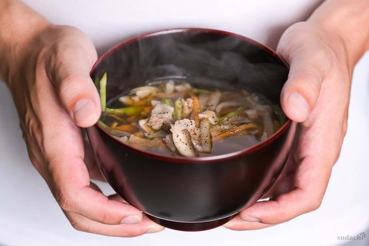 Yuto Omura holding up a bowl of homemade Japanese pork and vegetable soup with clear broth (sawaniwan)
