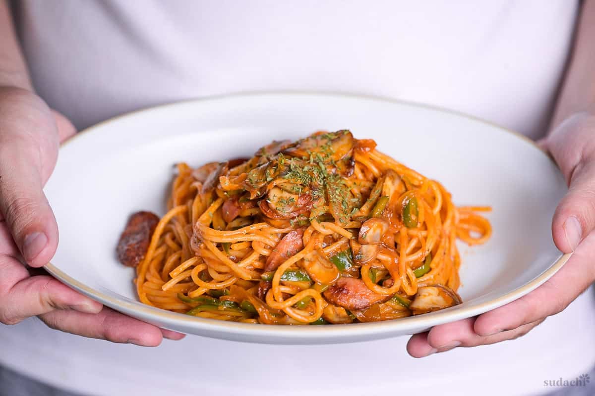Yuto Omura holding up Japanese Ketchup Spaghetti (Spaghetti Napolitan) on a white oval plate