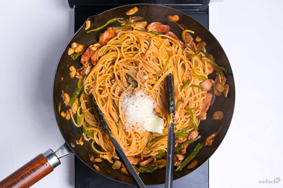 Spaghetti napolitan topped with butter, parmesan cheese and ground black pepper in a wok on the stove top.