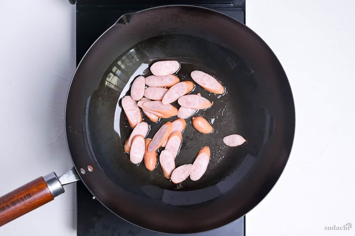 hot dog sausages frying in a wok on the stove top