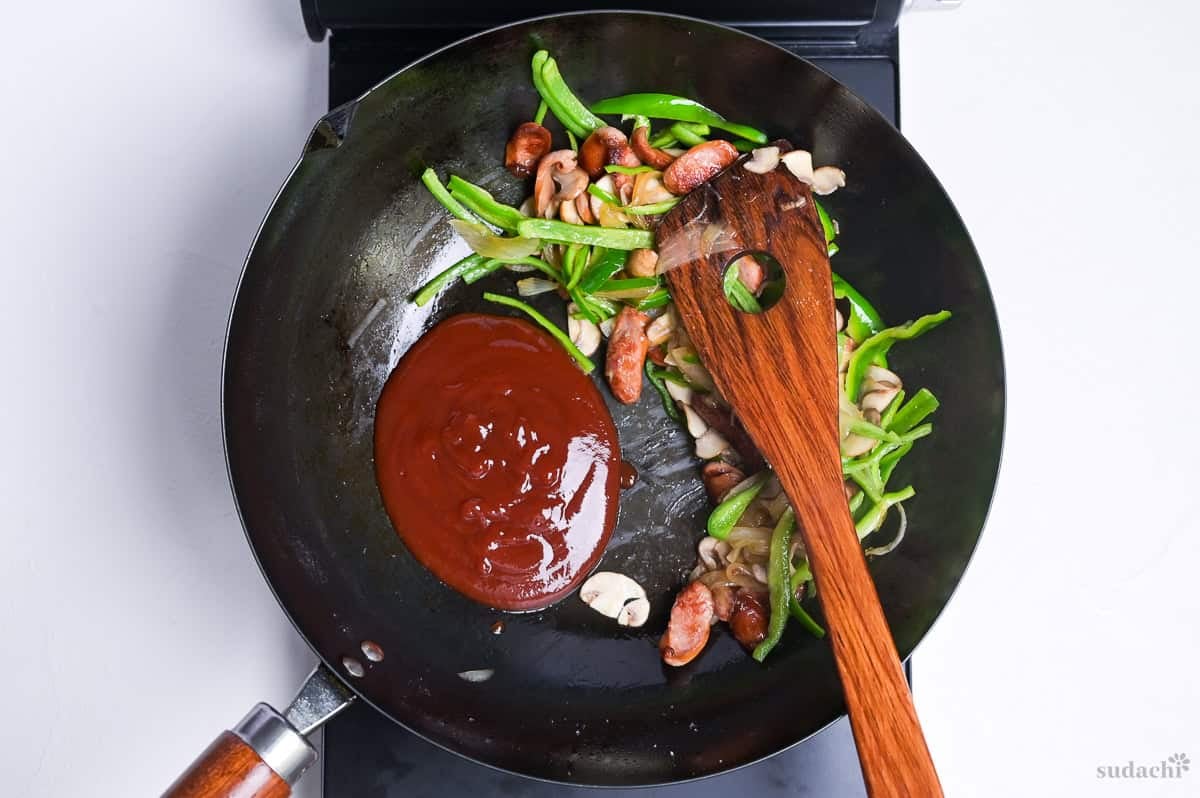 Sautéed spaghetti Napolitan ingredients pushed to the side of the wok with sauce in the empty space