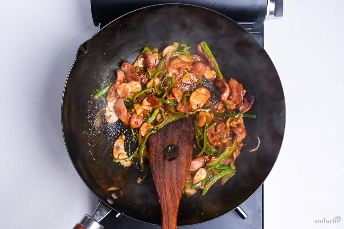 Ingredients and sauce for spaghetti napolitan mixed together in a wok on the stove top.