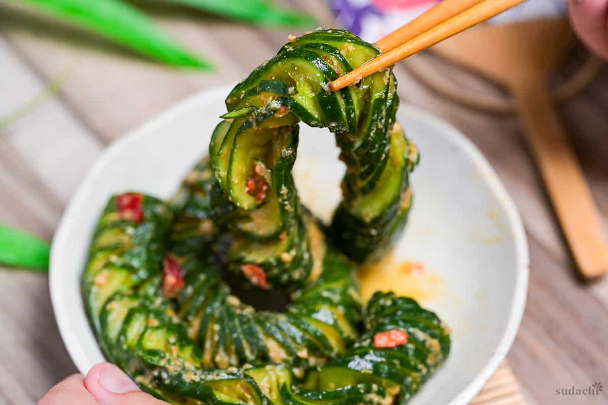 Spicy miso accordion cucumber salad lifted with light wooden chopsticks