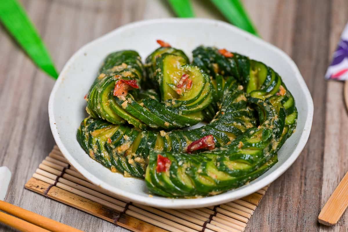Spicy miso accordion cucumber salad spiralling on a white dish side view