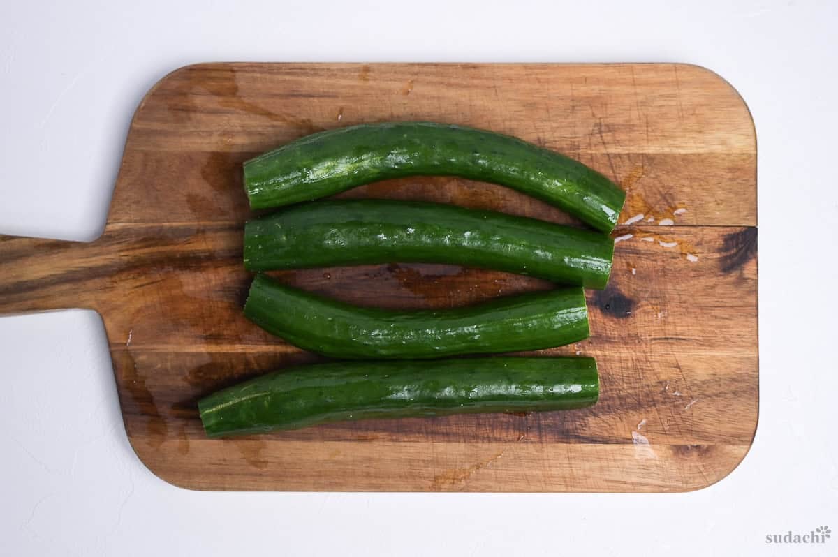 four Japanese cucumbers with the ends cut off on a wooden cutting board