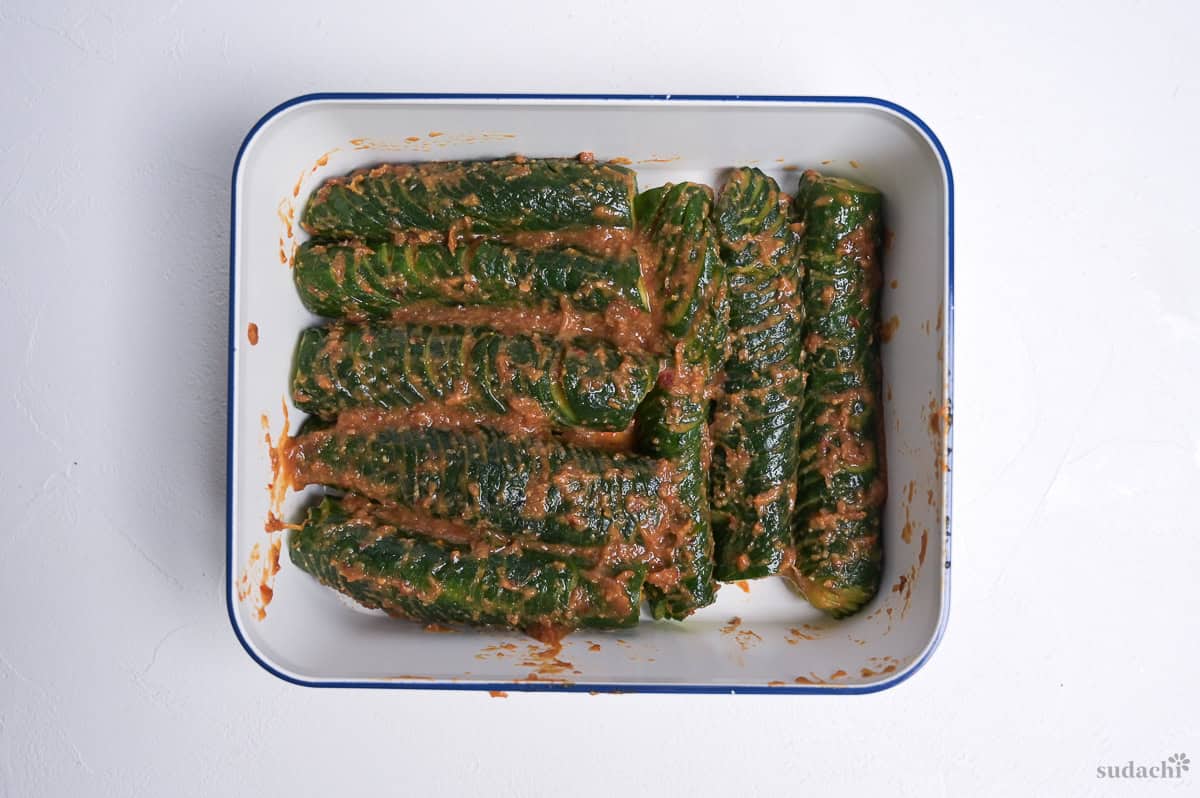 accordion cucumbers coated in spicy miso marinade in a white container with blue rim