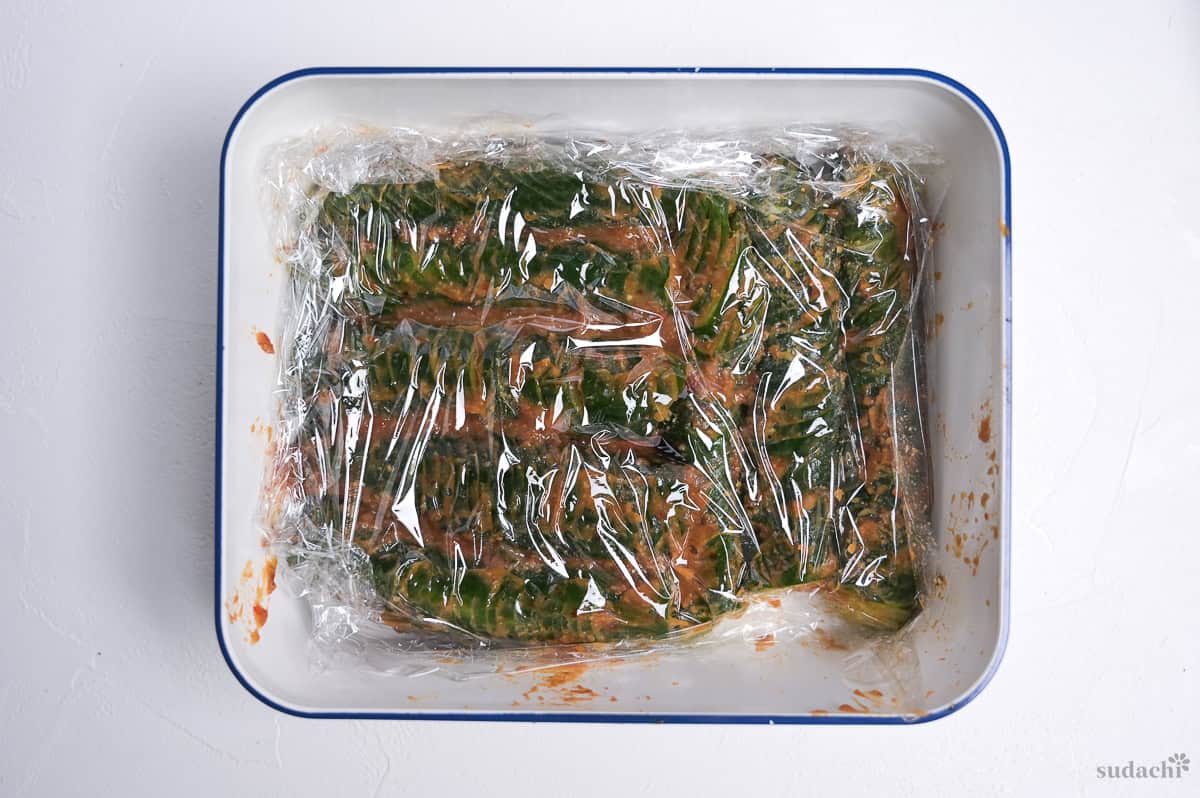 spicy miso accordion cucumbers in a container covered with plastic wrap
