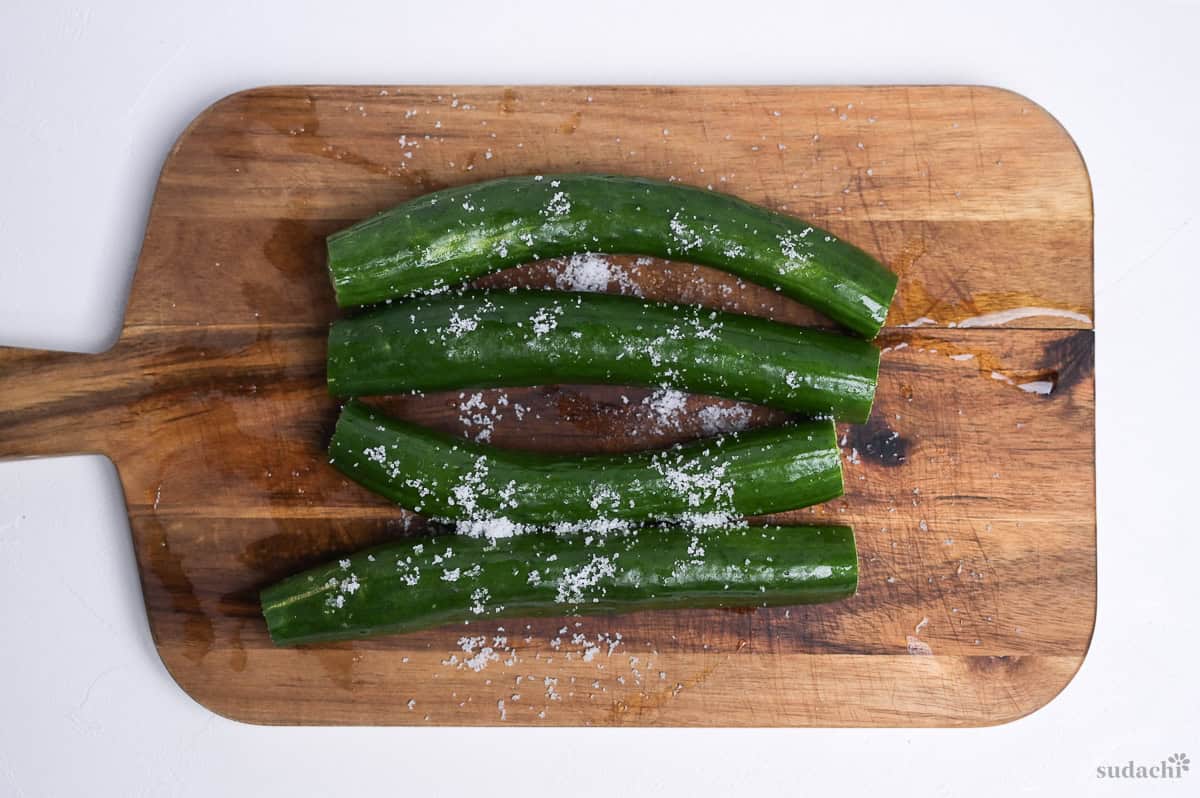 Four Japanese cucumbers sprinkled with coarse sea salt on a wooden cutting board