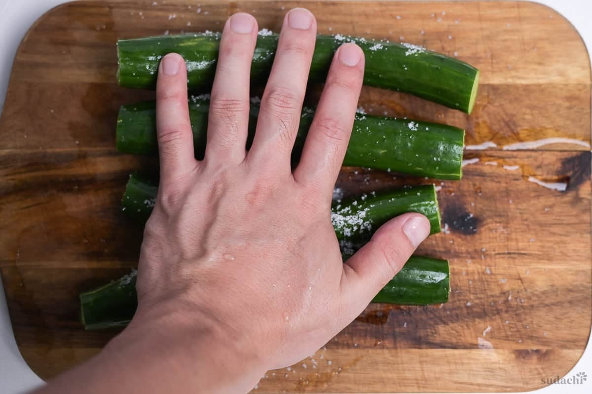 salt rubbing the surface of Japanese cucumbers on a wooden cutting board