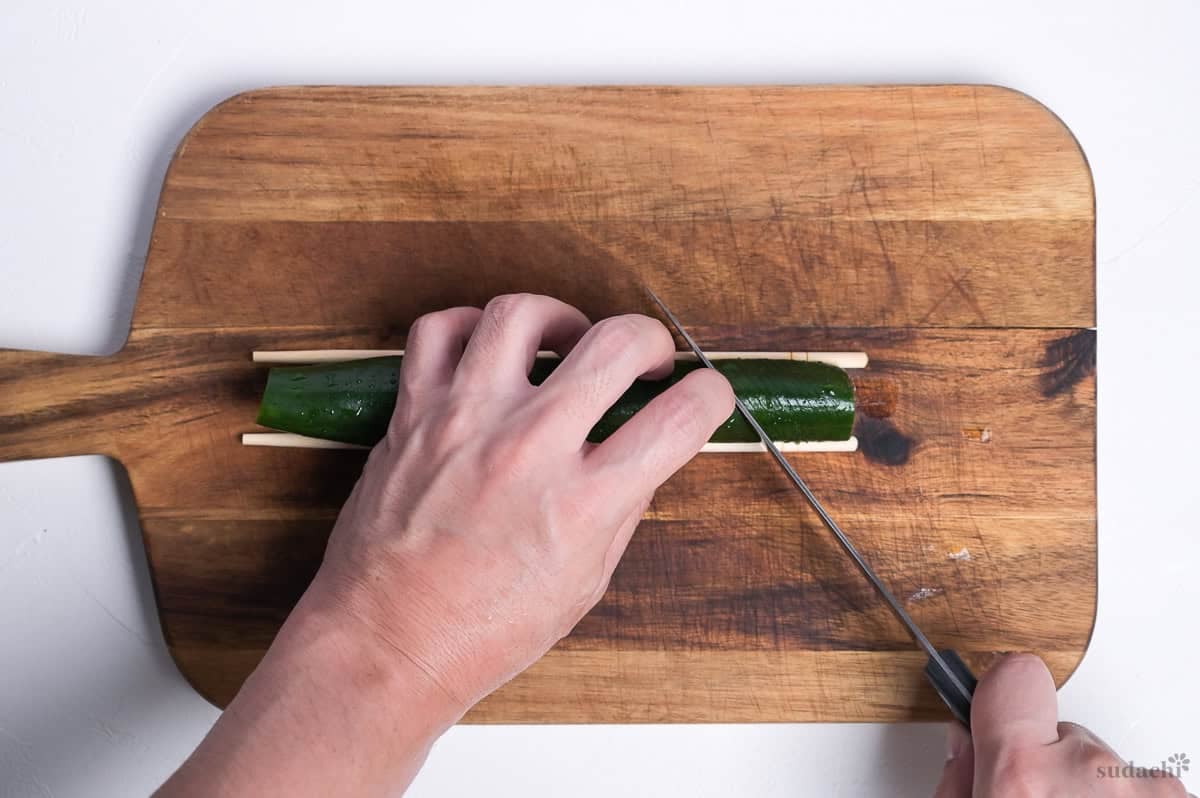 thinly slicing cucumber on the diagonal using chopsticks as a guide to make spicy miso accordion cucumbers