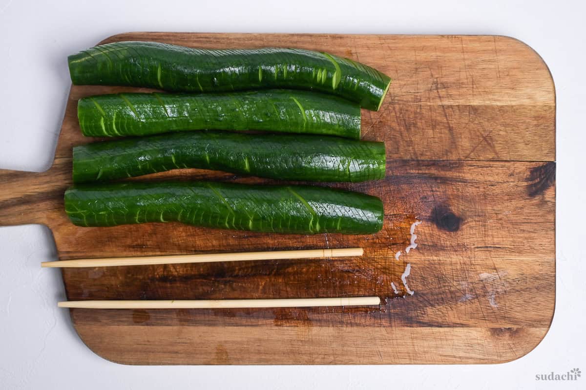 four Japanese cucumbers cut accordion style on a wooden cutting board