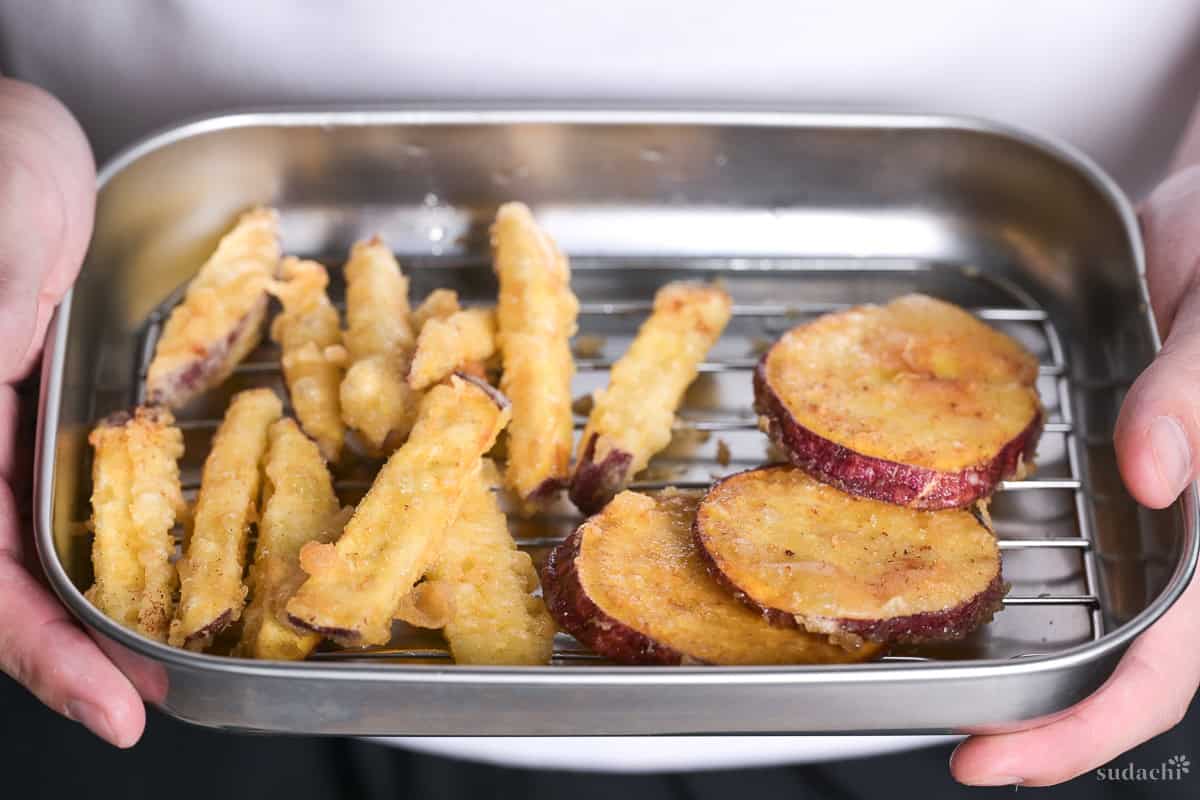 Yuto Omura holding up sweet potato tempura on a wire rack inside a steel container.