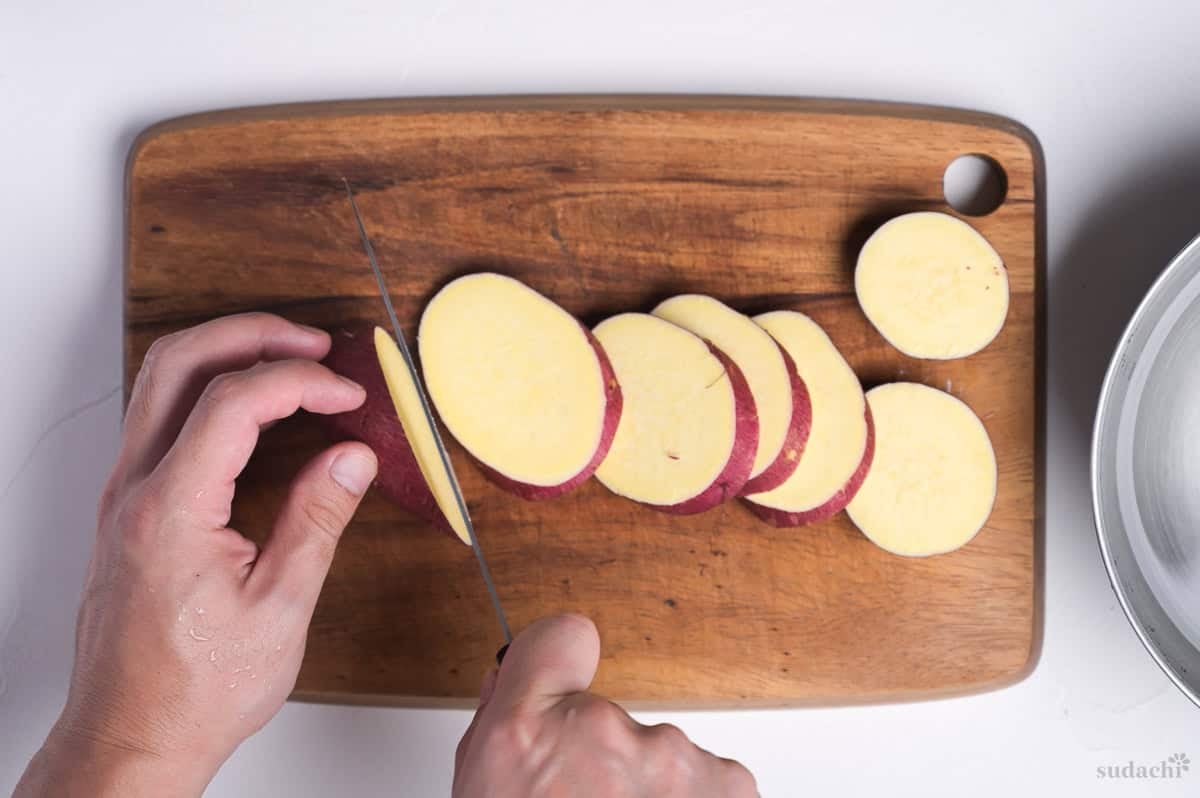 diagonally slicing Japanese sweet potato on a wooden cutting board