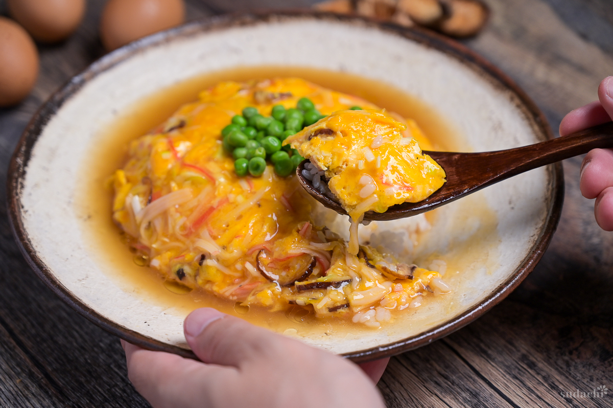A brown spoon taking a scoop of tenshinhan (Japanese crab omelette with rice) topped with green peas served on a textured cream plate with brown rim