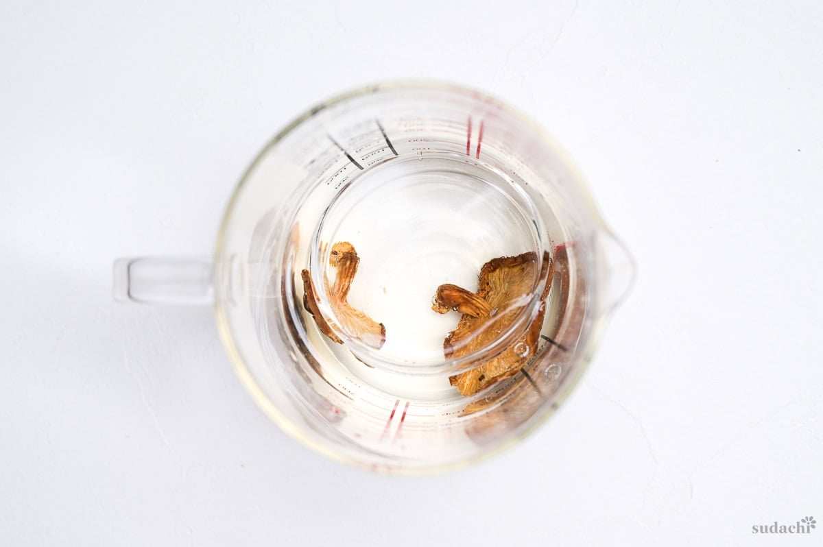 Two dried shiitake mushrooms in a jug of water weighed down with a small glass bowl to rehydrate the mushrooms and make shiitake dashi