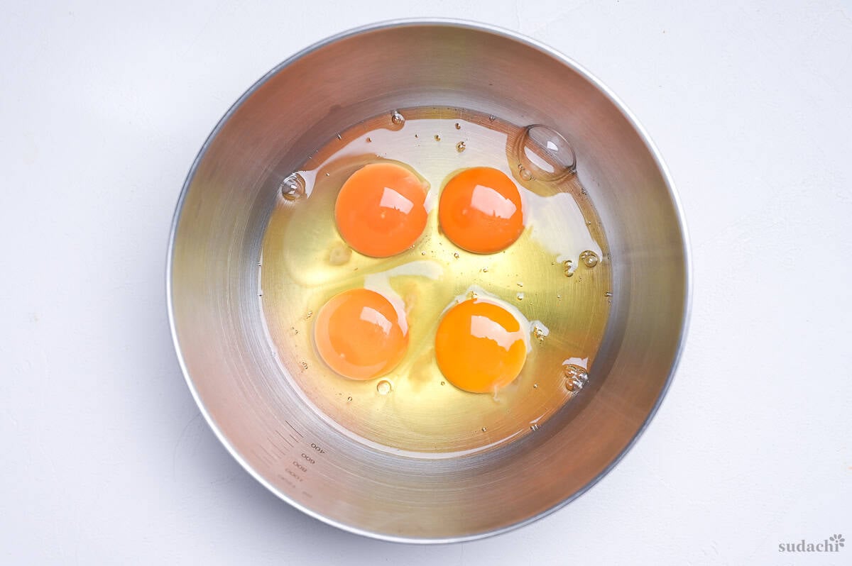 Four eggs cracked into a silver mixing bowl