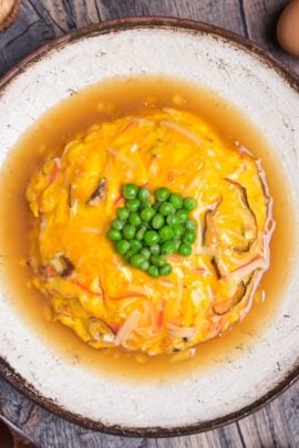 tenshinhan (Japanese crab omelette with rice) topped with green peas served on a textured cream plate with brown rim