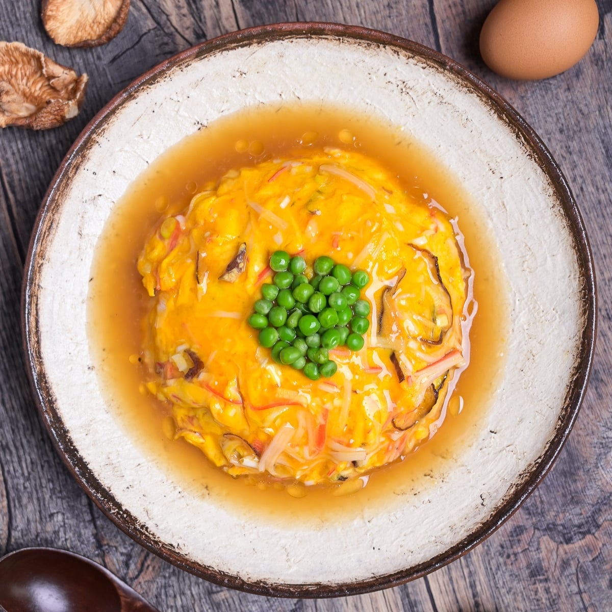 tenshinhan (Japanese crab omelette with rice) topped with green peas served on a textured cream plate with brown rim