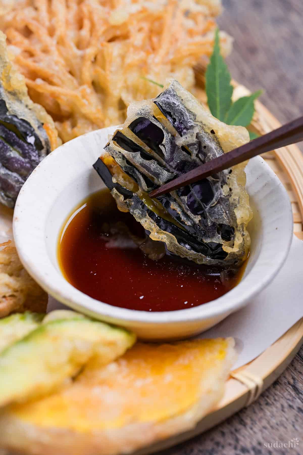 dipping a piece of eggplant tempura in homemade tentsuyu tempura dipping sauce