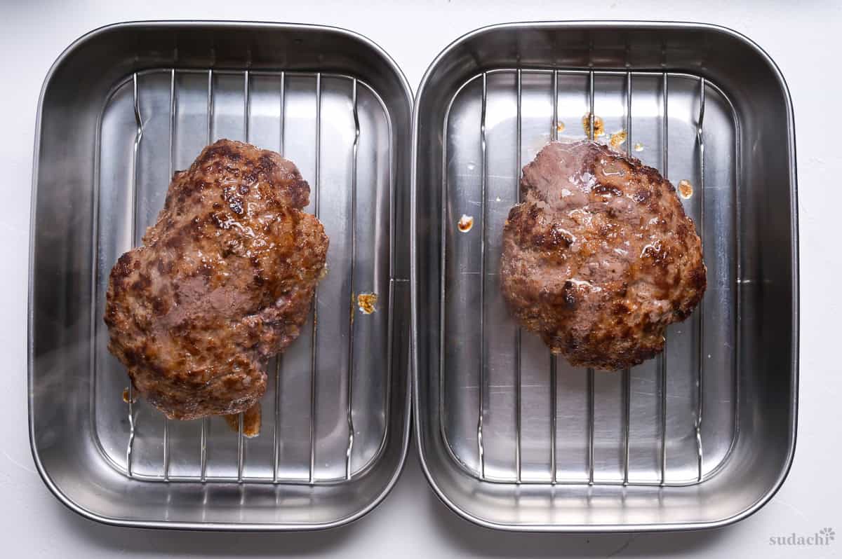 resting two pan fried wafu hamburgs on wire racks in containers side by side